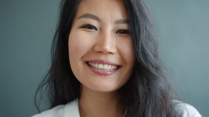 A woman with long dark hair smiles warmly at the camera against a soft gray background
