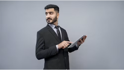 A man in a dark suit holds a tablet and looks ahead as he prepares for a session