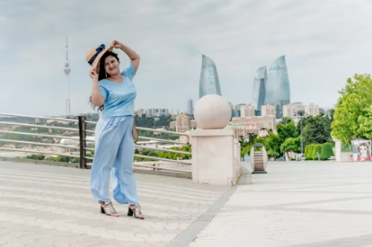 A woman stands confidently on an open plaza with a city skyline behind her